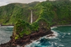 a tendril-like rock formation coming into the ocean and a waterfall flowing into the ocean seem from just above the ocean on Maui's Hana & Haleakala Helicopter Tour in Hawaii USA.
