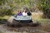 Two women in their Mucky Duck vehicle splash through muddy water