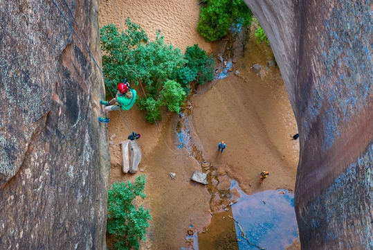 Looking down from the top of a rappel point at someone rappeling down the rock face on the Moab Canyoneering Adventure Moab Utah.
