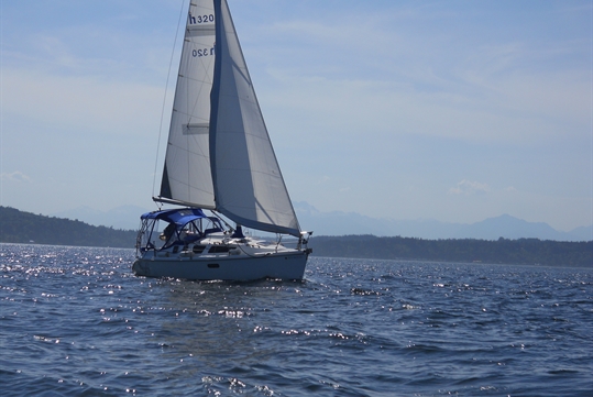 The sail boat out on the water with the mountains behind it on the Private Sailing Adventure on the Puget Sound in Seattle Washington USA.